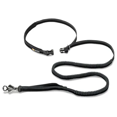 Sort hundesnor og sele med kliklås, mærketekst 'RUFFWEAR' synlig på både snor og sele. Materiale: tekstil med metalspænde på snoren.