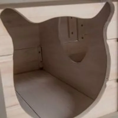 Træhus med indgang formet som kattehoved, synlig indvendig bund og vægge i lyst træmateriale. Ingen tekst eller mærker synlige.