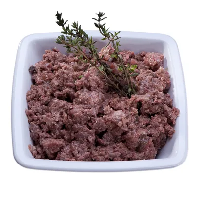 Миска с влажным кормом для животных, сверху украшена веточками зелени. Видны кусочки мясной массы розово-коричневого цвета.