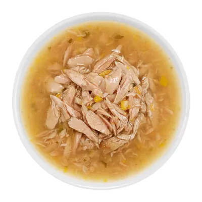 Nahaufnahme von zerkleinertem Fleisch in Brühe mit gelben und grünen Gemüsestücken, serviert in einer weissen Schale.