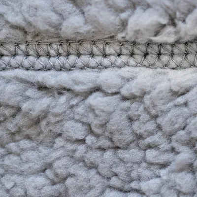 Gros plan sur une couture et la texture d’un tissu gris en polaire ou fausse fourrure, matière douce visible pour accessoires ou couchages pour animaux.