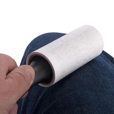 Luddroller med svart handtag används på mörkblått tyg, synlig pappersyta med ludd och hår fastnade.