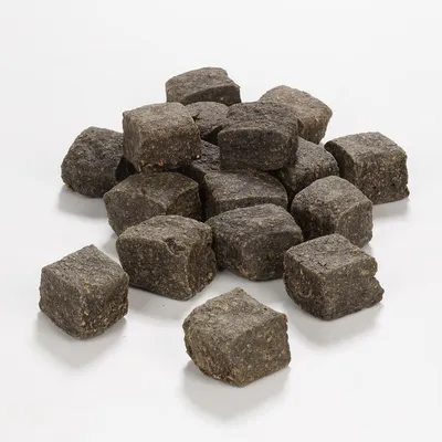Morceaux cubiques de friandises brunes pour animaux, sans emballage ni marque visible, posés sur une surface blanche.