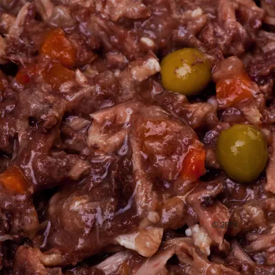 Cibo umido per animali con pezzi di carne, carote arancioni e olive verdi visibili in primo piano.