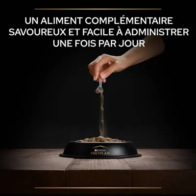 Un aliment complémentaire savoureux et facile à administrer une fois par jour. Main versant une poudre sur des croquettes dans une gamelle Purina Pro Plan.