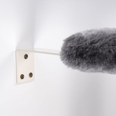Grijs, pluizig object bevestigd op een witte wandhouder met drie schroeven.