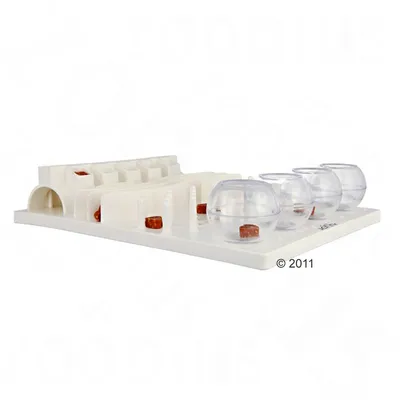 Plateau d’activité blanc avec plusieurs modules en plastique, dont des sphères transparentes et des compartiments, contenant des friandises visibles à différents endroits.