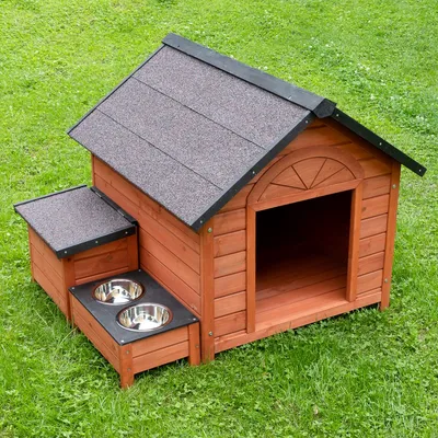 Houten hondenhok met zwart dak, zijwaarts voedergebied en twee roestvrijstalen voerbakken. Staat op een groen grasveld.