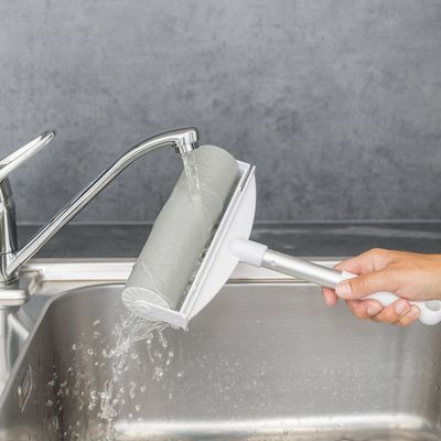 Hand hält eine Fusselrolle mit abwaschbarem Design unter fliessendem Wasser am Waschbecken. Zeigt einfache Reinigung der Rolle.