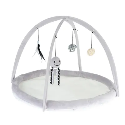 Tapis de jeu rond avec arches en tissu gris, quatre jouets suspendus dont une peluche souriante, une boule argentée, une boule beige et un jouet à plumes noires et blanches.