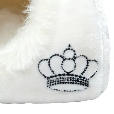 Entrée d'une niche ou maison pour animal en tissu blanc, bordure en fausse fourrure blanche, broderie noire en forme de couronne visible sur le côté.