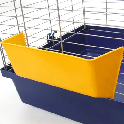 Gelber Futternapfaufsatz aus Kunststoff, befestigt an einem blauen Käfig mit Metallgitter.