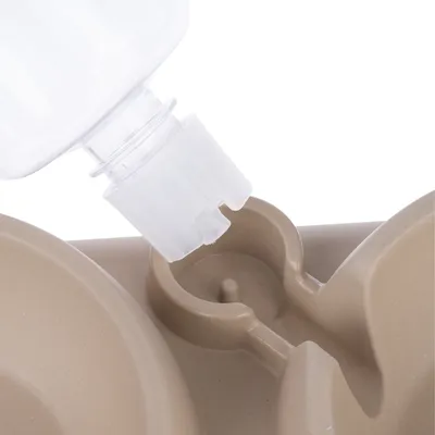 Close-up of a beige food bowl with water bottle holder. Shows attachment of a transparent bottle to the bowl.