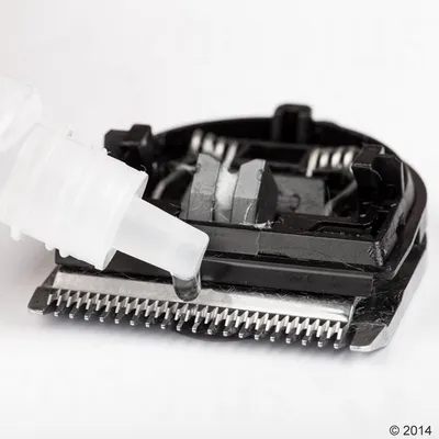Nahaufnahme einer Schermaschine mit Tropfen Schmieröl auf den Klingen, zeigt die Pflege und Wartung des Geräts.