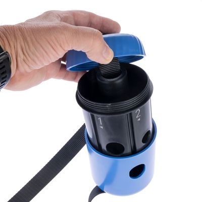 Χέρι ανοίγει μπλε δοχείο με μαύρο εσωτερικό, αριθμημένο με 1 και 2. Διακρίνονται τρύπες και αποσπώμενος ιμάντας.