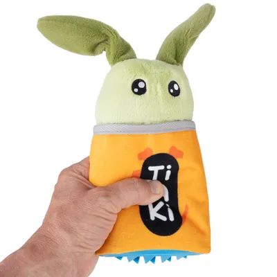 Hand håller ett grönt plyschleksak med öron och orange hölje, med texten 'TiKi'.