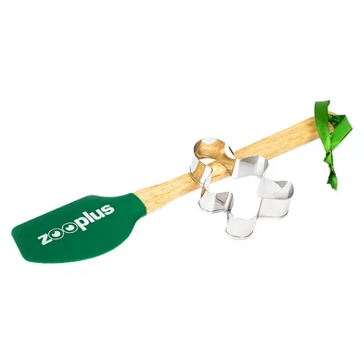 Utensílio de pastelaria Zooplus com raspador de silicone verde, cabo de madeira e cortador de metal em forma de osso, decorado com fita verde.