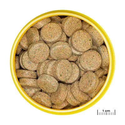 Pyöreät ruskeat ruokatabletit keltaisessa purkissa, oikeassa alakulmassa mitta näyttää 1 cm koon vertailua varten.
