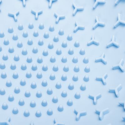 Surface en plastique bleu avec picots ronds au centre et motifs en forme de Y autour, vue rapprochée du relief visible.