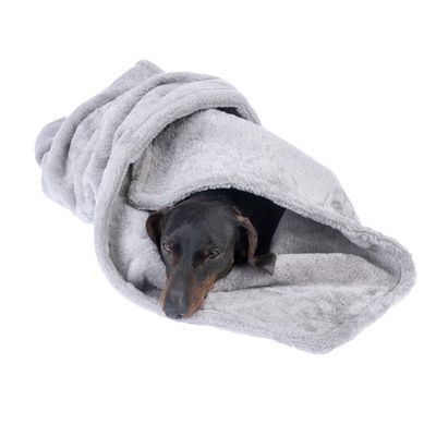 Koira makaa harmaassa pehmeästä materiaalista tehdyssä vilttipedissä, sopii nukkumiseen tai käpertymiseen.