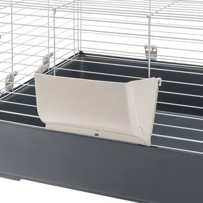Vue d’une cage pour rongeur avec bac en plastique gris et mangeoire beige fixée aux barreaux métalliques blancs.