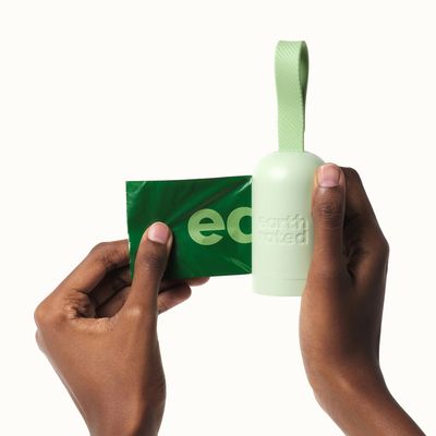 Distributeur vert clair avec lanière et sachet vert, marque visible : earth rated. Deux mains tiennent le distributeur et tirent un sac.