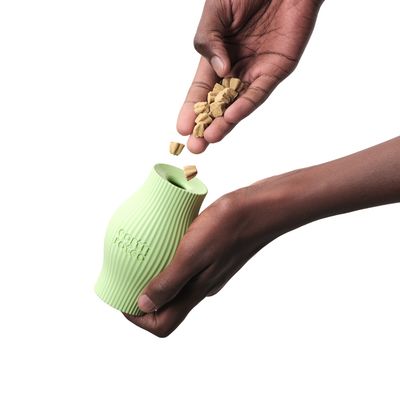 Zelená, vroubkovaná láhev na krmivo s nápisem 'corn raised', naplněná malými pamlsky z ruky.