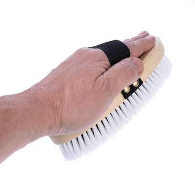 Ръка държи четка с дървена дръжка и бели косъмчета, снабдена с черна каишка за захващане.
