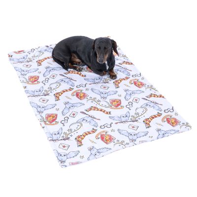 Hund ligger på en vit filt med Harry-Potter-motiv som ugglor, vapen och glasögon.