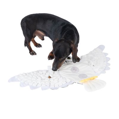 Куче играе с бялa подложка за душене във формата на птица, подходяща за занимание и търсене на храна.