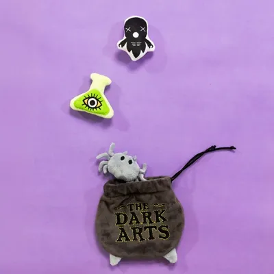 Jouets en peluche pour animaux : une araignée grise sortant d’une pochette noire avec texte « THE DARK ARTS », un flacon vert avec œil et une figurine noire à tête de mort. Jouets en peluche pour animaux : une araignée grise sortant d’une pochette noire avec texte « THE DARK ARTS », un flacon vert avec œil et une figurine noire à tête de mort.