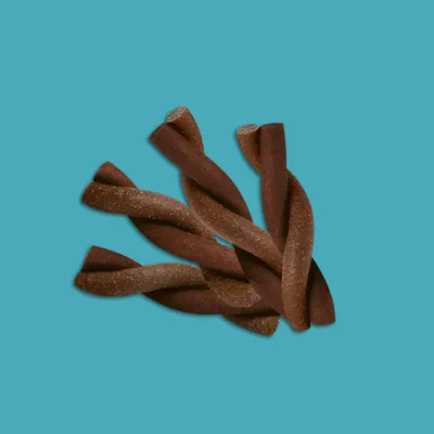 Bâtonnets torsadés bruns, friandises pour animaux, présentés en vrac sur fond uni bleu. Aucun emballage ni marque visible.
