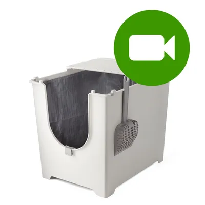 Plastikowa kuweta dla kota z szarą łopatką zawieszoną z boku, wewnątrz widoczna ciemnoszara wkładka. Zielona ikona kamery w prawym górnym rogu.