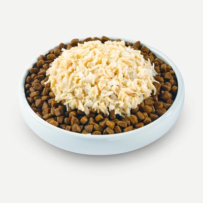 White bowl with brown dry food pieces, topped with a portion of shredded light-coloured meat.