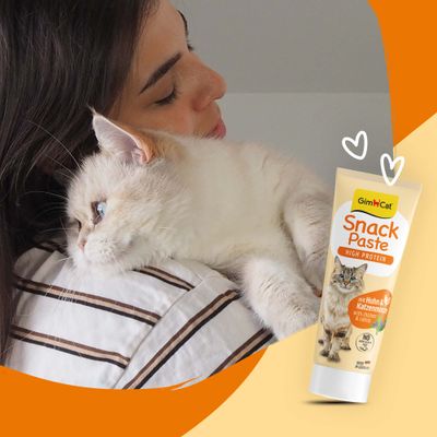 GimCat Snack Paste High Protein med kyckling och kattmynta, tub med kattbild, bredvid en katt på en axel.