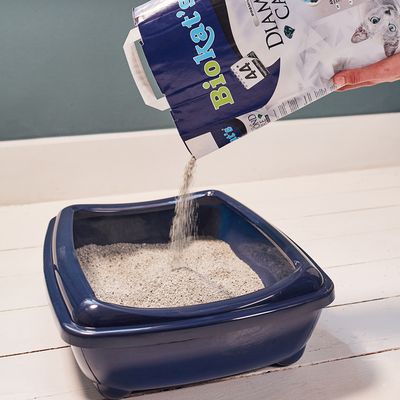 Biokat's Diamond Care kattenbakvulling wordt in een blauwe kattenbak gegoten. Verpakking met productnaam en zichtbare kat.