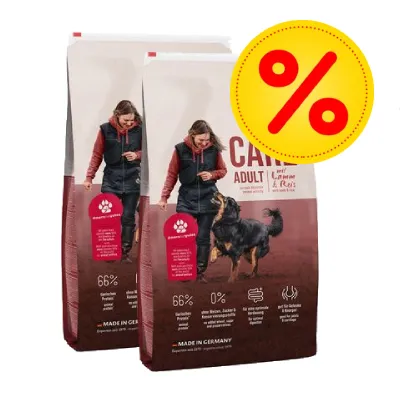 Två säckar hundfoder med texten 'ADULT', synlig procent-symbol för rabatt, 66 % animaliskt protein, 0 % spannmål, MADE IN GERMANY. Bild på person och hund på förpackningen.