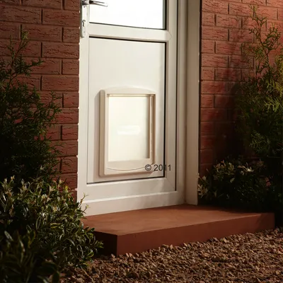 Porta bianca con sportello per animali SureFlap integrato, circondata da mattoni rossi e piante.