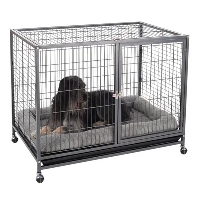 Hond in een metalen kooi met traliewanden, grijs kussen en wielen. Kooi met zichtbare deur en sluiting.