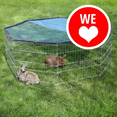 Recinto ottagonale in metallo con copertura a rete, due conigli all'interno su prato. Cerchio rosso con testo bianco 'WE' e cuore visibile in alto a destra.