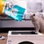 Sanicat Clumping cat litter is poured into a litter tray while a grey cat stands next to it.