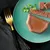 Close-up of served wet food on a green plate, garnished with parsley. Shows texture and presentation of the food.