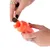 Una mano riempie un gioco arancione con snack rotondi. Dimostrazione dell’uso di un distributore di cibo per pet.