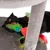 Chat noir allongé sur un arbre à chat gris, tenant un jouet en tissu rouge avec des plumes vertes, bleues et jaunes visibles.