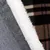 Widok szczegółowy szarego materiału z białą, puszystą krawędzią na tle w kratkę.