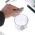 Hand opening transparent container with grey lid, part of a kooa device. Cable and device visible in the background.