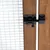 Gros plan sur un loquet en métal noir fixé sur une porte en bois avec grillage métallique à mailles carrées visibles.