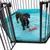 Schwarzer Metall-Laufstall mit türkisfarbener Matte und rotem Spielzeugknochen. Hund steht in der Mitte des Laufstalls.