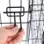 Fermeture en métal d'une cage grillagée, main tenant le loquet pour ouvrir ou fermer la porte. Structure en métal noir visible en gros plan.