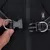 Gros plan sur une attache en plastique noir avec anneaux métalliques sur harnais, main tenant la boucle. Marque visible : TIAKI.